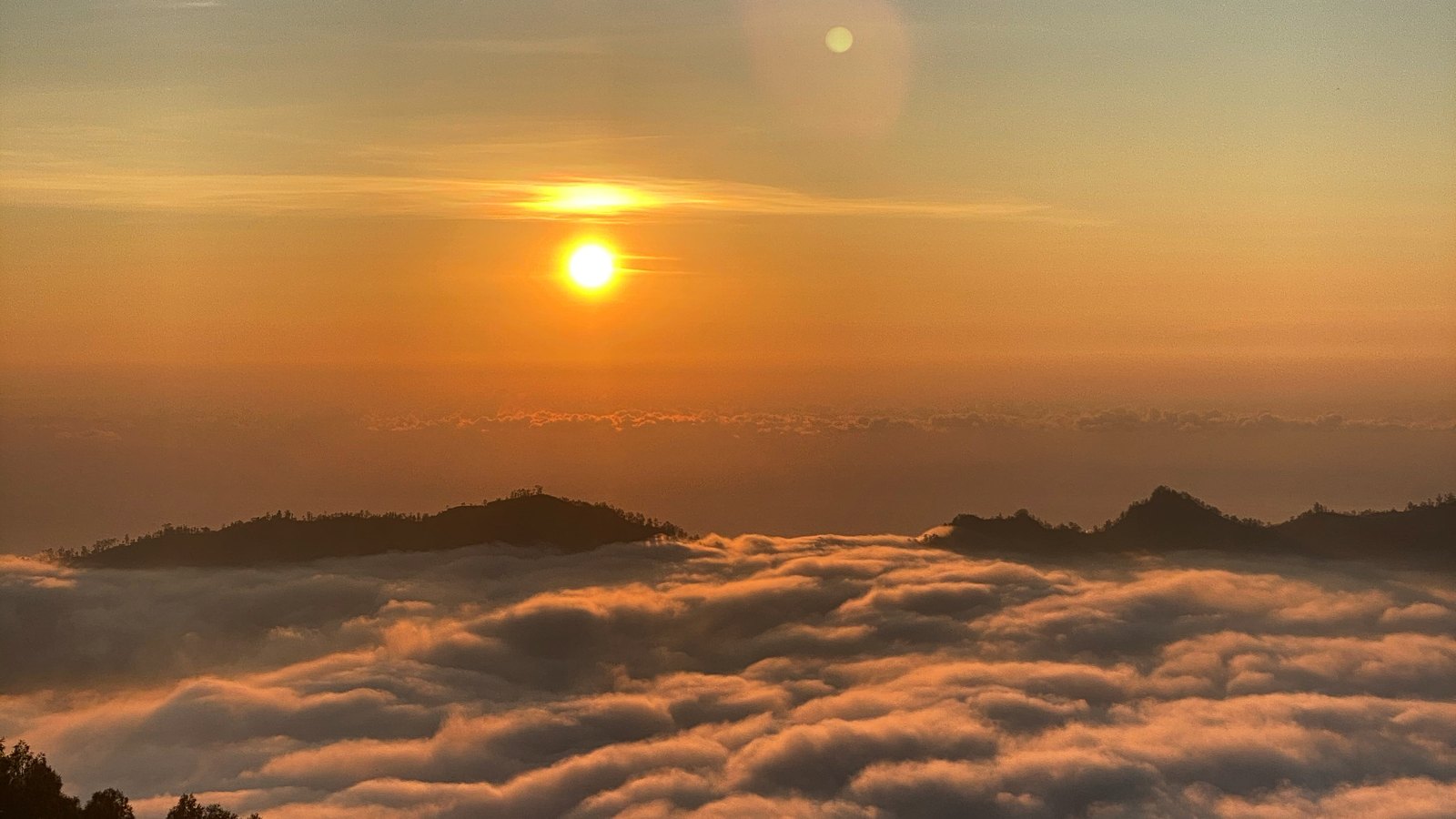 Sunrise from Mount Batur above a sea of cloud: the sun just clear of the horizon in an orange sky, ridgelines standing out of the cloud layer below
