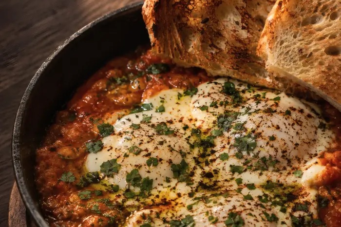 Shakshuka in a cast-iron pan: eggs baked in tomato sauce with herbs and toasted sourdough on the side, at Shaffa GastroBazar in Balangan